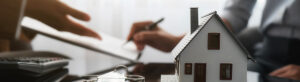 Representação de um contrato imobiliário sendo assinado, com uma miniatura de uma casa em primeiro plano e chaves ao lado, simbolizando a transação de imóveis e a securitização de multipropriedades.