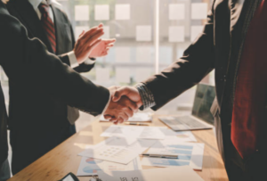 Aperto de mãos entre executivos em um ambiente corporativo, simbolizando parceria e confiança na escolha da securitizadora ideal para um projeto, com documentos financeiros e gráficos na mesa.