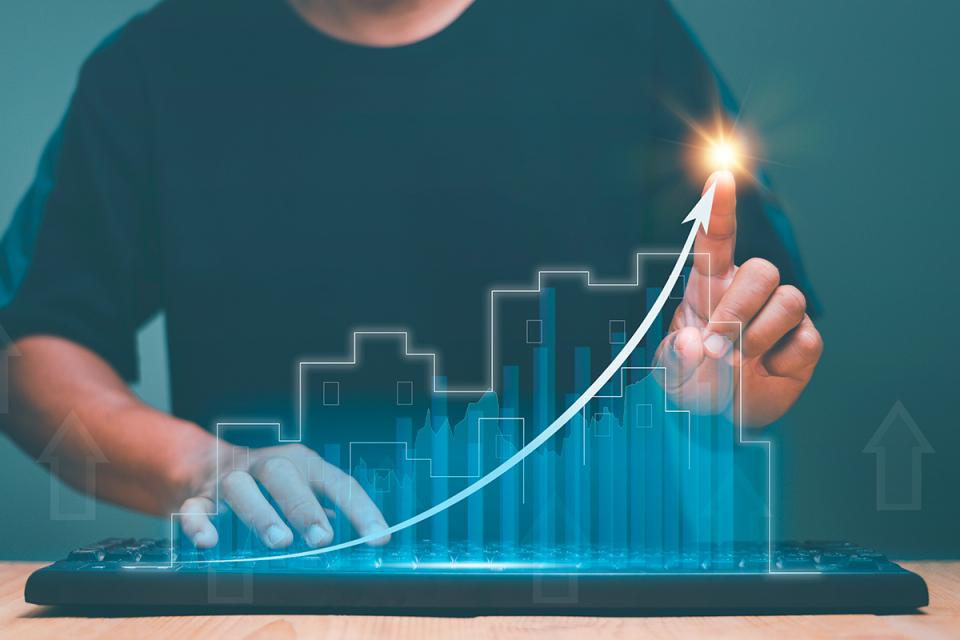 Pessoa usando teclado com gráfico digital de crescimento e edifícios ao fundo, simbolizando o avanço do setor imobiliário e a diversificação de funding via mercado de capitais.